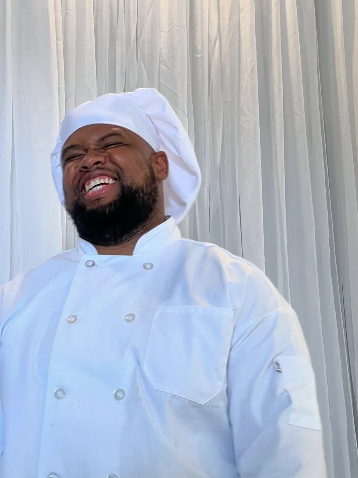 Chef Brandon Timberlake laughing in his white chef coat and hat