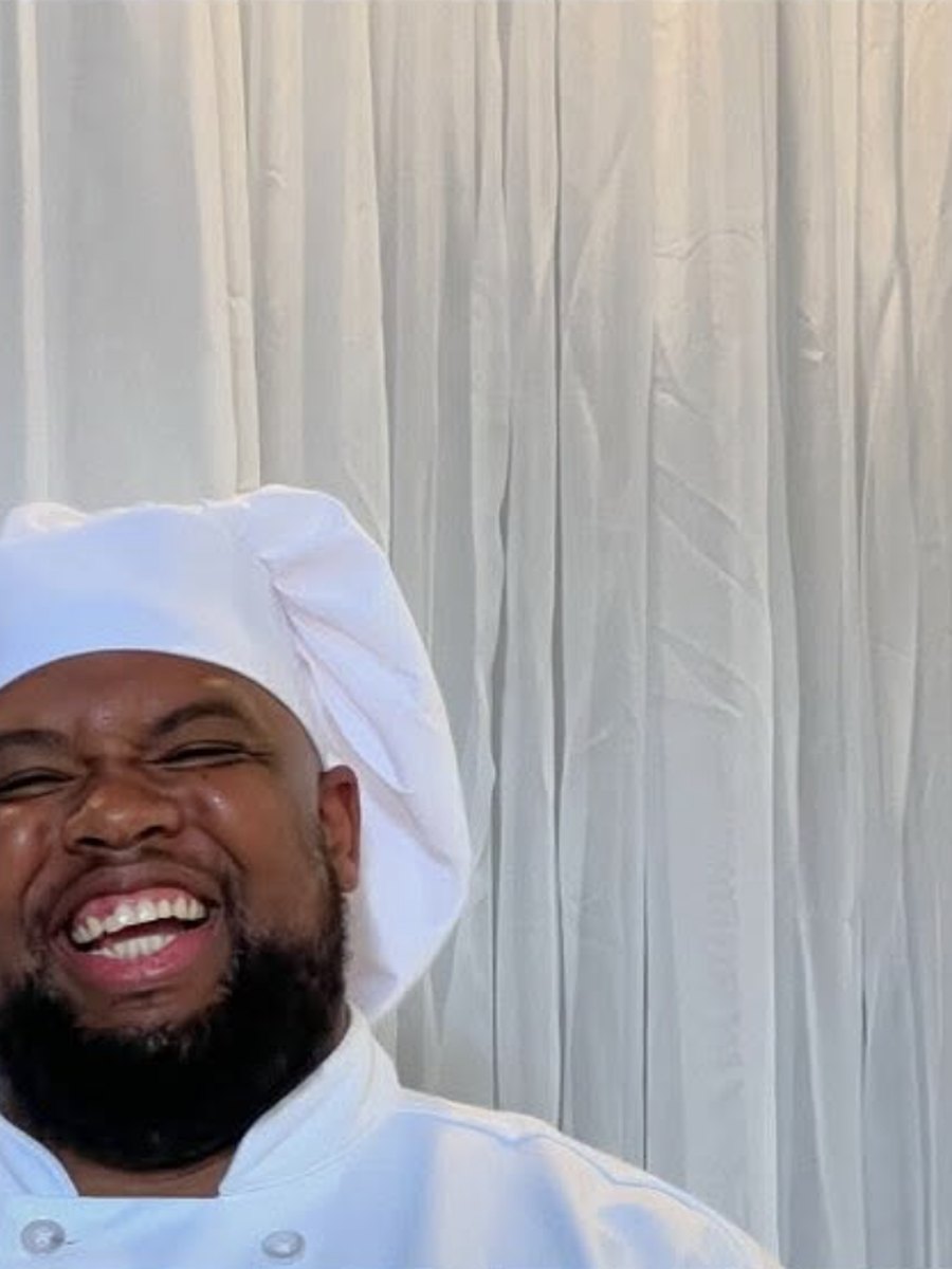Chef Brandon laughing, white coat against a curtain backdrop