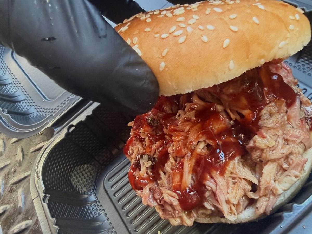 Pulled pork sandwich with sauce on a sesame bun, held with a black glove