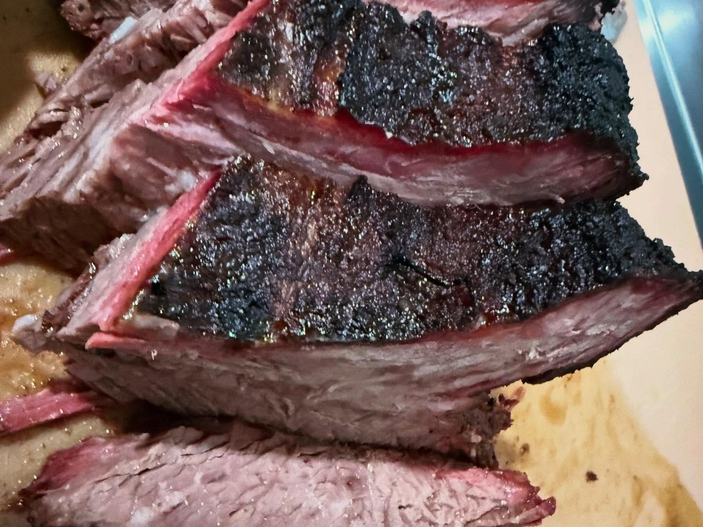 Sliced smoked brisket with a deep bark and pink smoke ring, cut thick on a board